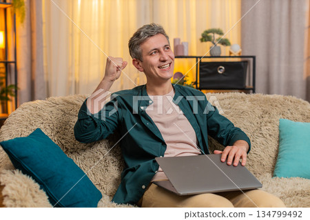 Young man closes laptop with smile and shows victory gesture after finishing productive online work Young man closes laptop with smile and shows victory gesture after finishing productive online work 134799492