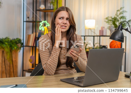 Young woman touches cheek feels tooth pain searches dentist contacts on smartphone and books online 134799645