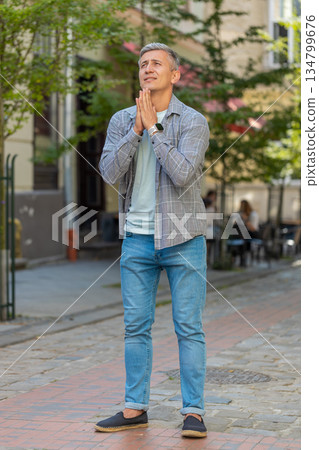Caucasian mature man tourist praying with closed eyes to God asking for blessing on city town street 134799676