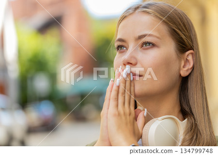 Young Caucasian woman meditating, breathes deeply with hands clasped, praying eyes closed on street Young Caucasian woman meditating, breathes deeply with hands clasped, praying eyes closed on street 134799748