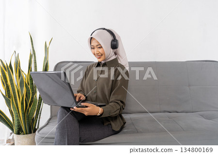 woman with headscarf learning on laptop with headphones woman with headscarf learning on laptop with headphones 134800169