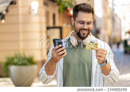 Man using credit bank card smartphone while transferring money, purchases online shopping outdoors Man using credit bank card smartphone while transferring money, purchases online shopping outdoors 134800299