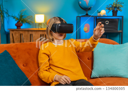 Teenager boy child excitedly playing VR, waving hands, showing WOW emotion, sitting on sofa at home 134800305