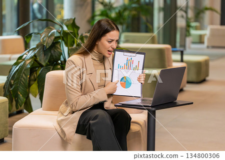 Angry young woman boss arguing over video call in office showing diagram charts reports on laptop Angry young woman boss arguing over video call in office showing diagram charts reports on laptop 134800306