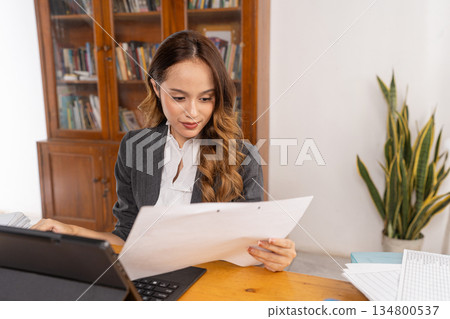 Concentrated female professional examining paperwork diligently Concentrated female professional examining paperwork diligently 134800537