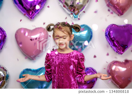 Confetti and glitter fly on the person. balloons in the shape of hearts in the background of a child. A happy, positive girl enjoys the moment. 134800818