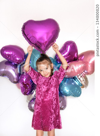 A lovely smiling beautiful girl holds a foil balloon in the shape of a heart above her, Happy Valentine's Day. The worldwide like symbol in social media and web communication 134800820