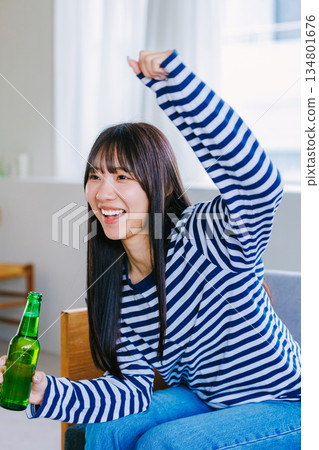 年輕女子在家喝啤酒看運動比賽 134801676