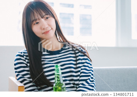 年輕女子在家中客廳喝啤酒 年輕女子在家中客廳喝啤酒 134801711