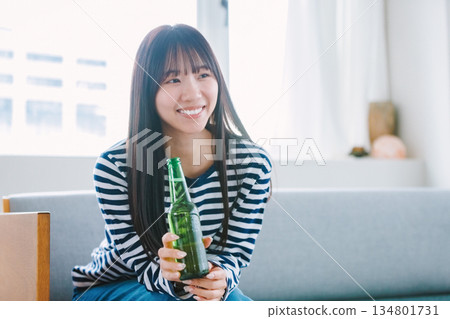 年輕女子在家中客廳喝啤酒 134801731