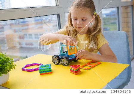 A child's creative play session with magnetic building blocks is captured against a bright yellow backdrop, showing various constructed shapes. A child's creative play session with magnetic building blocks is captured against a bright yellow backdrop, showing various constructed shapes. 134804146