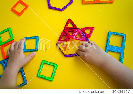 A child's creative play session with magnetic building blocks is captured against a bright yellow backdrop, showing various constructed shapes. A child's creative play session with magnetic building blocks is captured against a bright yellow backdrop, showing various constructed shapes. 134804147