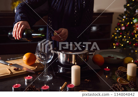 Winter Holiday Kitchen Scene With Woman Pouring Wine, Spices, Candles, And Christmas Tree Winter Holiday Kitchen Scene With Woman Pouring Wine, Spices, Candles, And Christmas Tree 134804842