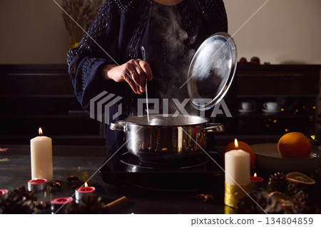 Winter Dinner Scene: Woman in Evening Gown Preparing Mulled Wine by Candlelight 134804859