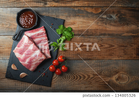 Raw pork ribs with spices, salt and rosemary on dark wooden background Raw pork ribs with spices, salt and rosemary on dark wooden background 134805326