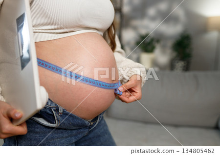 Pregnant woman measures her growing belly with a tape measure, tracking progress during pregnancy 134805462