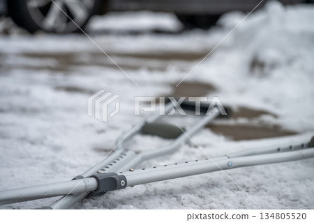 Crutches rest on snowy ground outside a car during winter weather in the late afternoon Crutches rest on snowy ground outside a car during winter weather in the late afternoon 134805520