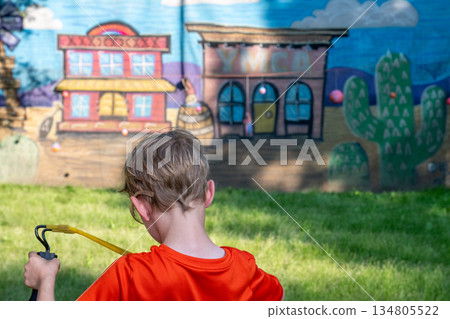 Child playing with a slingshot in a park near colorful mural during a sunny afternoon in a suburban area 134805522
