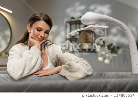 Young mother gazes fondly at a baby mobile with plush toys hanging above crib, anticipating motherhood Young mother gazes fondly at a baby mobile with plush toys hanging above crib, anticipating motherhood 134805534