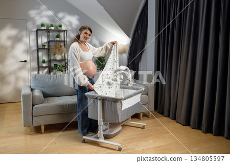 Expecting mother arranges bedding in bedside bassinet, anticipating newborn arrival in cozy home nursery setting Expecting mother arranges bedding in bedside bassinet, anticipating newborn arrival in cozy home nursery setting 134805597