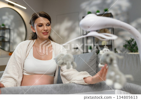 Expecting mother gazes at plush toys on crib mobile, anticipating newborn's arrival in cozy nursery setting 134805613