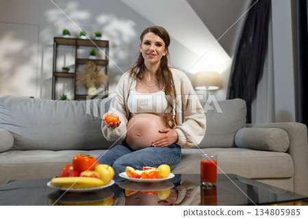 Expecting mother sits on sofa with fruit and juice, enjoying healthy snack during pregnancy 134805985