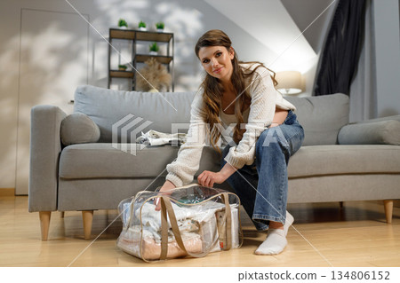 Expecting mother prepares for childbirth by organizing clothes and essentials in a transparent bag at home Expecting mother prepares for childbirth by organizing clothes and essentials in a transparent bag at home 134806152