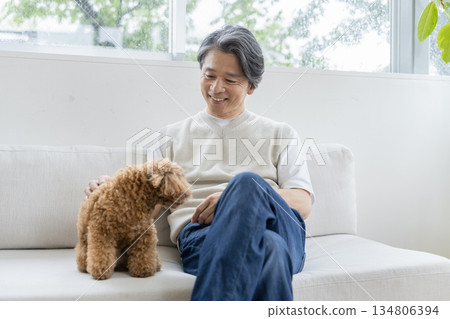 一位五十多歲的男子和他的狗一起在沙發上放鬆。這是與狗狗相伴生活的畫面。 一位五十多歲的男子和他的狗一起在沙發上放鬆。這是與狗狗相伴生活的畫面。 134806394