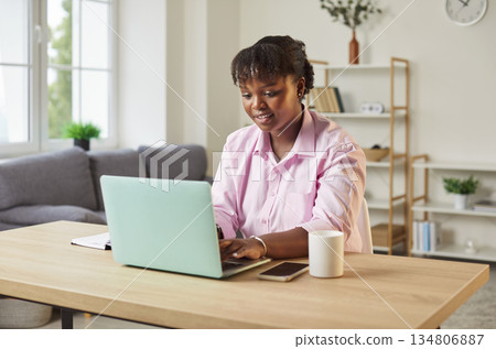 Young African American woman freelancer sitting at her desk and working on laptop Young African American woman freelancer sitting at her desk and working on laptop 134806887