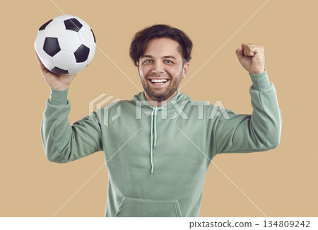 Cheerful male player having fun at soccer match, holding ball, raising fist up and smiling 134809242