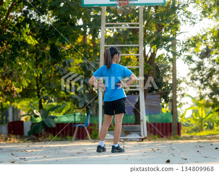 Young girl standing on outdoor basketball court in casual sportswear Young girl standing on outdoor basketball court in casual sportswear 134809968