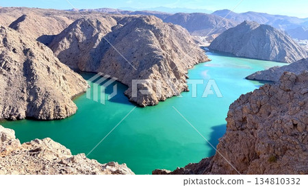 Emerald Cliffs Seen From Ridge, Turquoise Channel Snaking Between Rocky Promontories, Bright Sunlight And Calm Shoreline, Perfect For Kayaking Route Planning And Drone Conten 134810332