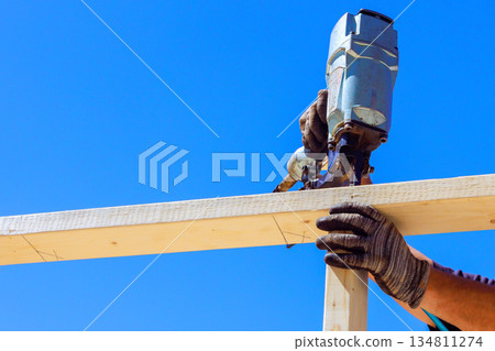 Worker holds wood in place while using pneumatic nail gun to build beams frame. Worker holds wood in place while using pneumatic nail gun to build beams frame. 134811274