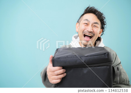 Smiling delivery person holding a delivery bag for food delivery, home delivery service work image, green background Smiling delivery person holding a delivery bag for food delivery, home delivery service work image, green background 134812538