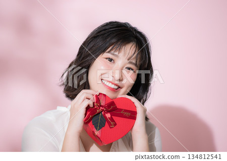 一位面帶微笑的女子手持情人節禮物。這幅畫面可能像徵著告白、活動或禮物。她正看向鏡頭。 134812541