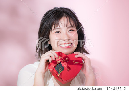 一位面帶微笑的女子手持情人節禮物。這幅畫面可能像徵著告白、活動或禮物。她正看向鏡頭。 134812542