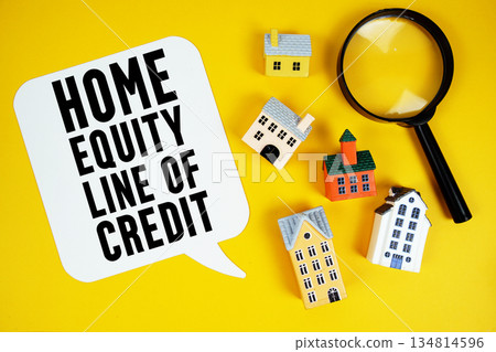 HELOC Home Equity Line of Credit text with house models and magnifying glass on yellow background HELOC Home Equity Line of Credit text with house models and magnifying glass on yellow background 134814596