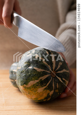 Hand holding kitchen knife and cutting green butternut squash on wooden board 134814699