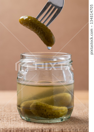 Pickled cucumber or Gherkin pickle in glass jar with fork on brown background Pickled cucumber or Gherkin pickle in glass jar with fork on brown background 134814705