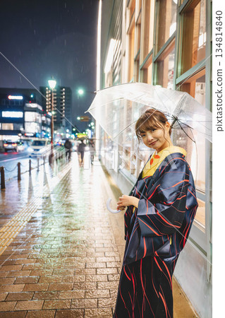 雨夜裡，一位身穿和服的年輕女子撐著傘站在街上。 134814840