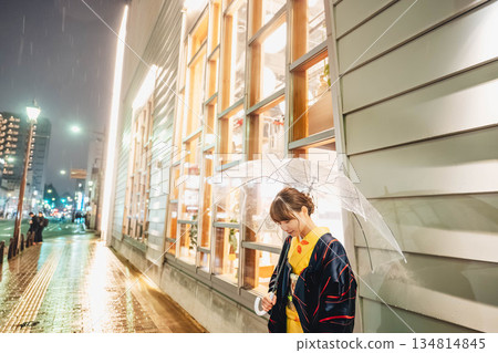 雨夜裡,一位身穿和服的年輕女子撐著傘站在街上。 雨夜裡,一位身穿和服的年輕女子撐著傘站在街上。 134814845