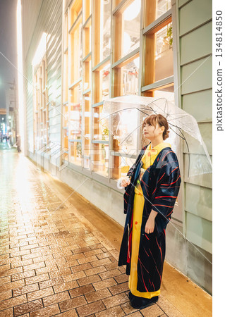 雨夜裡,一位身穿和服的年輕女子撐著傘站在街上。 雨夜裡,一位身穿和服的年輕女子撐著傘站在街上。 134814850
