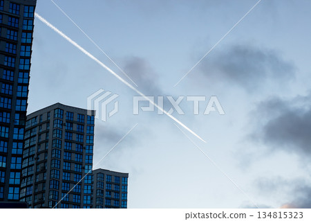 Cityscape with flying jet trail, Dusk city skyline showing airplane streaks and silhouettes 134815323