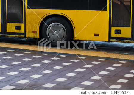 Closeup of yellow bus wheel and pavement, Detailed view of bus wheel on wet city pavement 134815324