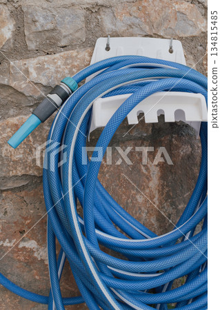 Garden hose coiled on wall mounted holder by stone wall 134815485