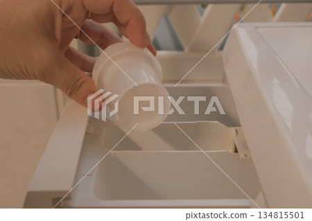 Female hand pouring fabric softener from cap into washing machine detergent compartment Female hand pouring fabric softener from cap into washing machine detergent compartment 134815501