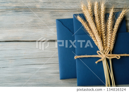 Handmade invitation set featuring navy blue envelopes with wheat embellishments and gold calligraphy on a rustic wooden surface 134816324