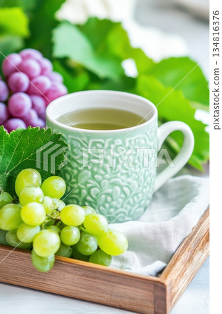 Cozy morning with herbal tea in a sage green ceramic cup and fresh green grapes on a wooden tray 134816376