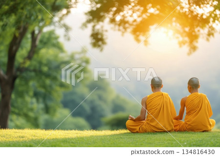 Group of Buddhist monks in saffron robes meditating in a serene forest clearing during soft morning light 134816430