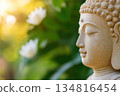 Intricately carved stone Buddha statue surrounded by lotus flowers in a lush garden bathed in gentle morning sunlight 134816454